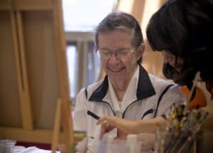 A Therapeutic Recreation Assistant helps a resident during art class.